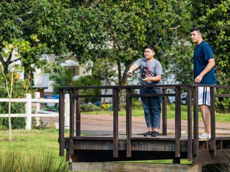 A scenic garden area featuring a wooden footbridge and a white picket fence, set within a well-maintained residential landscape.