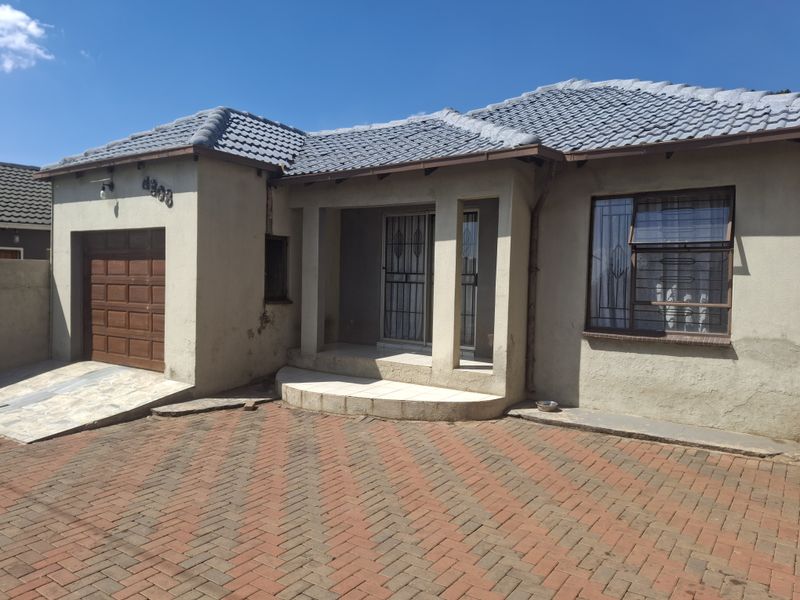 Front elevation of a single-story house featuring a tiled roof, integrated garage, paved driveway, and security features on windows and entrance.