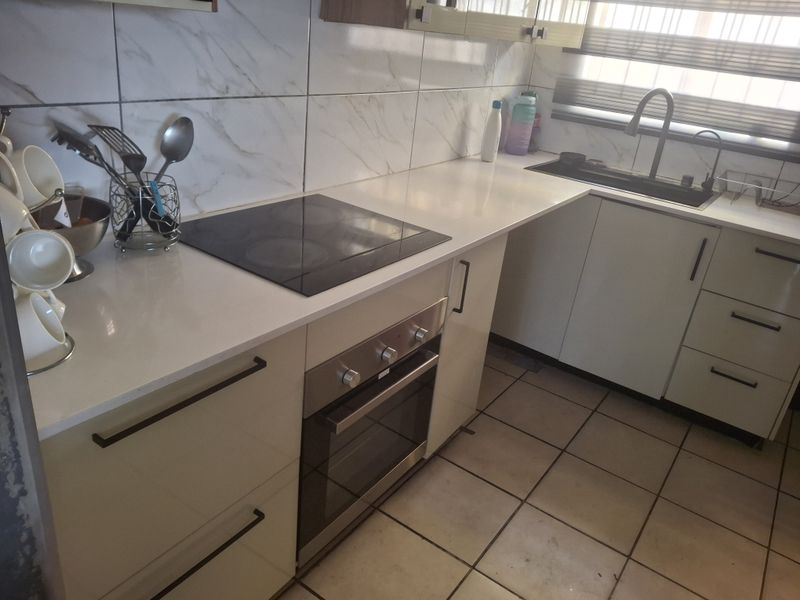 Modern kitchen featuring sleek cabinetry, quartz countertops, built-in oven, electric hob, and marble-look wall tiling with an undermount sink.