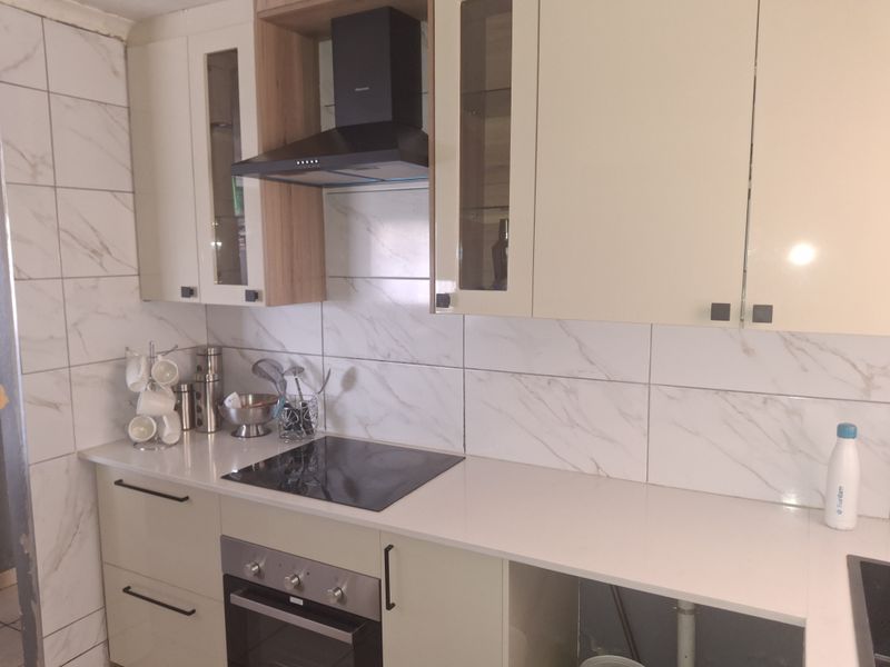 Modern kitchen featuring marble-look wall tiles, quartz countertops, built-in oven, and hob, with contemporary cabinetry and an integrated extractor fan.