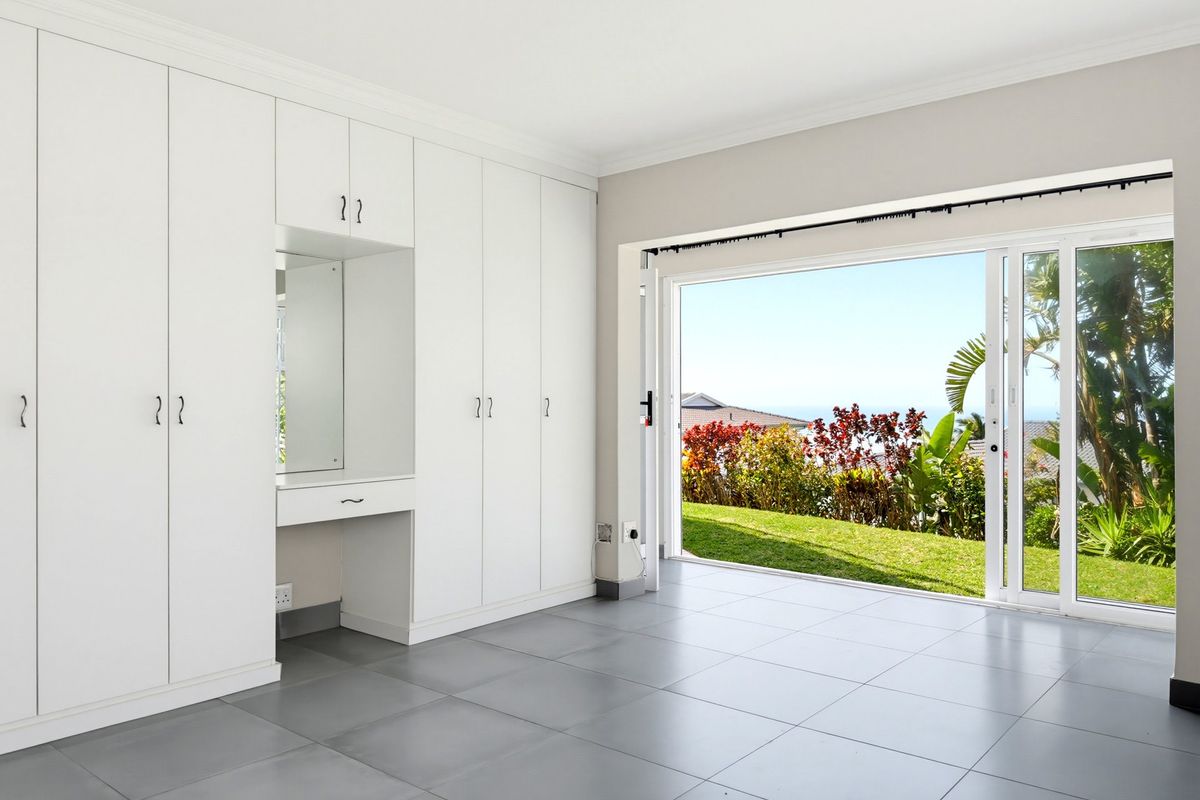 Spacious bedroom featuring extensive built-in cabinetry with a vanity station, large sliding glass doors, and neutral tiled flooring with direct garden access.