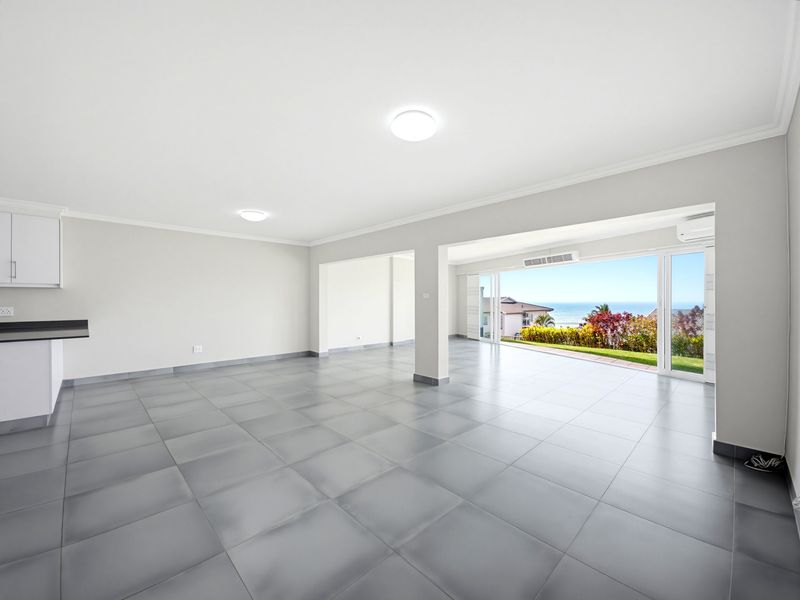 Spacious open-plan living area featuring large sliding glass doors that open to a scenic ocean view, complemented by neutral tiled flooring and modern finishes.