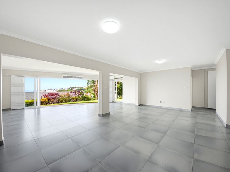 Spacious open-plan living area featuring neutral tiled flooring, modern ceiling lighting, and large sliding glass doors opening to an outdoor view.