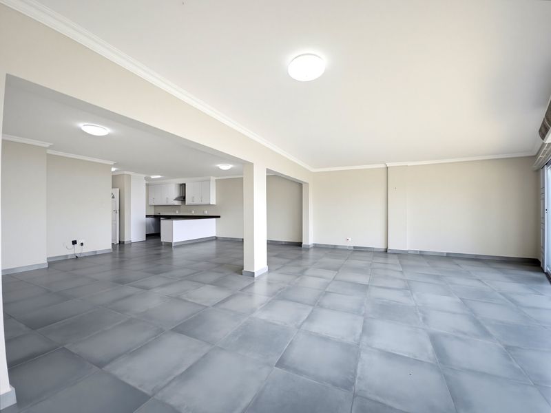 Spacious open-plan living area featuring large format floor tiles, neutral walls, and a modern kitchen with built-in cabinetry and breakfast counter.