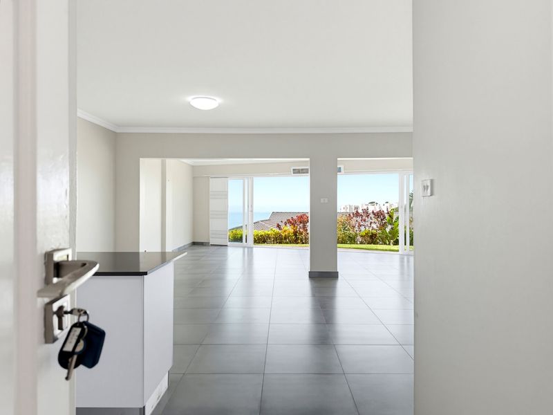 A bright, open-plan living area featuring large sliding glass doors that open to an outdoor view, complemented by neutral tiled flooring and a kitchen island.