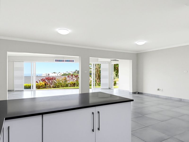 Spacious open-plan living area featuring modern tiled floors, a central kitchen island, and large sliding doors opening to a scenic outdoor view.