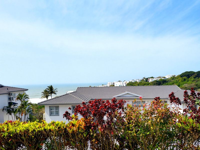 A scenic elevated view overlooking coastal residential buildings with tiled roofs and lush surrounding greenery under a clear blue sky.