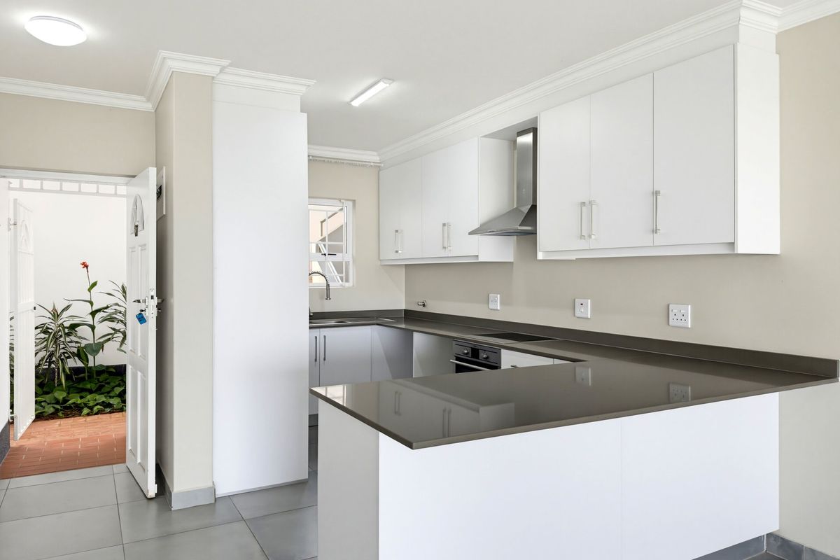 Modern kitchen featuring white cabinetry, stone countertops, built-in oven, hob, and extractor fan, with direct access to an outdoor courtyard area.