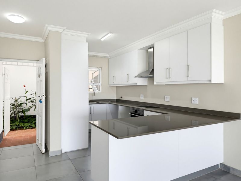 Modern kitchen featuring white cabinetry, stone countertops, built-in oven, hob, and extractor fan, with direct access to an outdoor courtyard area.
