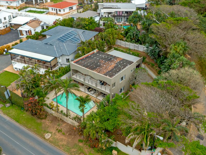 Aerial view of a residential property featuring a swimming pool, multi-level balconies, and solar panels on the roof, set within a landscaped garden.