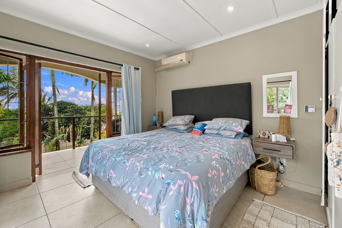 Spacious bedroom featuring tiled flooring, a split-system air conditioner, and large sliding glass doors opening onto a private balcony with garden views.