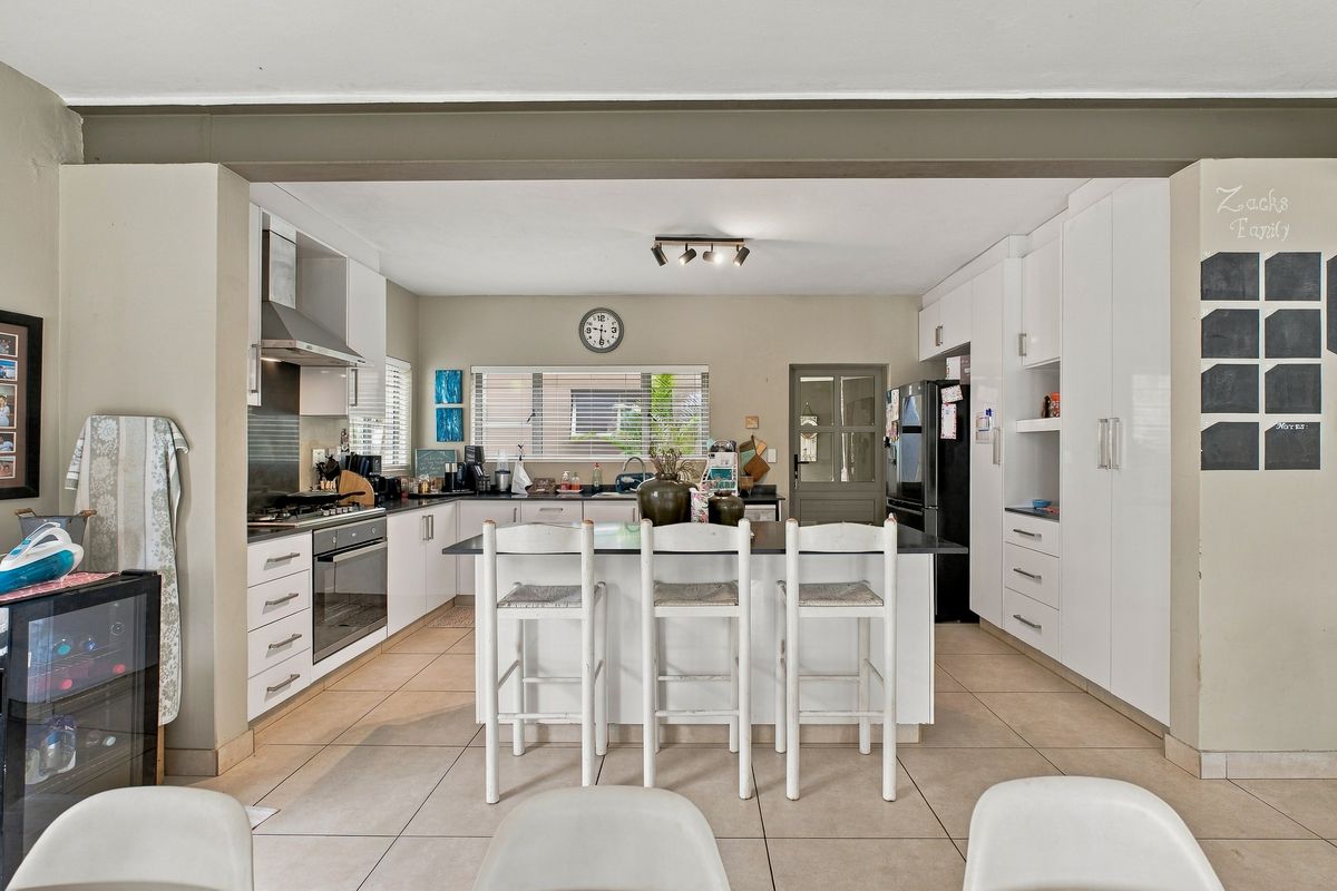 A modern open-plan kitchen featuring white cabinetry, a central island with seating, tiled flooring, and integrated appliances.
