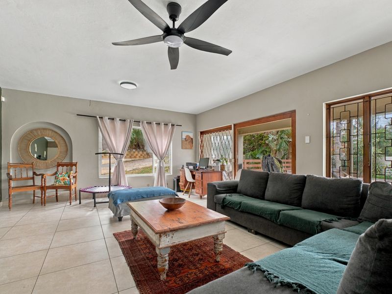 Spacious living room featuring neutral tiled flooring, a modern ceiling fan, and large sliding glass doors providing access to the outdoor area.