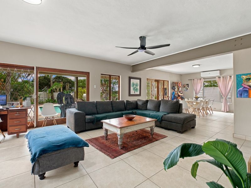 Spacious open-plan living and dining area featuring tiled floors, ceiling fans, and large sliding doors providing direct access to the outdoor pool area.