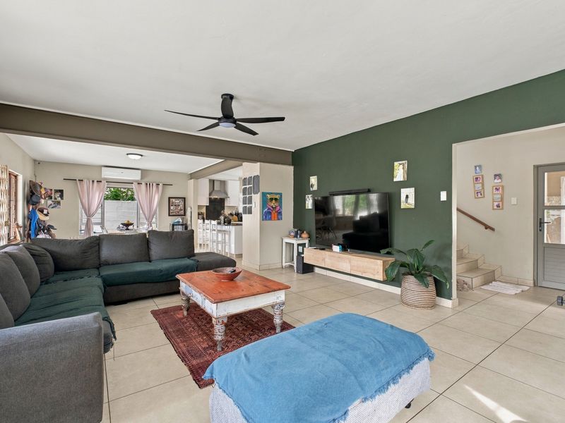 Spacious open-plan living area featuring tiled floors, a ceiling fan, and a seamless flow into the kitchen, with an adjacent staircase.