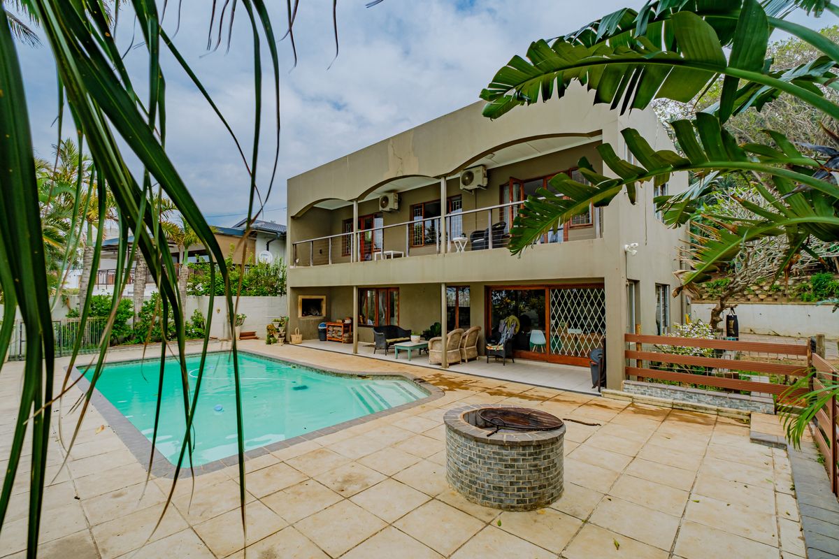 Rear exterior view featuring a swimming pool, paved patio area with a brick fire pit, and a two-story building with a balcony and built-in braai.