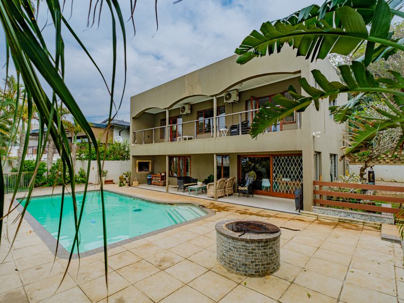 Rear exterior view featuring a swimming pool, paved patio area with a brick fire pit, and a two-story building with a balcony and built-in braai.