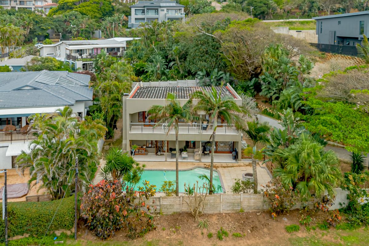 Aerial view of a multi-level residential property featuring a swimming pool, ground-floor patio, and upper-level balcony surrounded by lush garden landscaping.