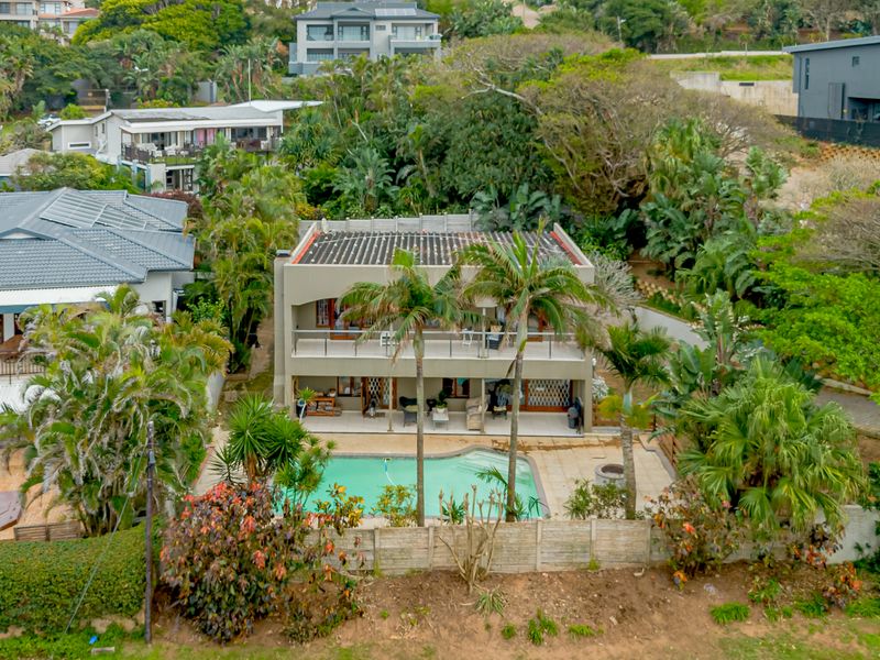 Aerial view of a multi-level residential property featuring a swimming pool, ground-floor patio, and upper-level balcony surrounded by lush garden landscaping.