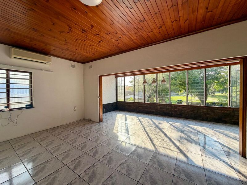 Spacious living area featuring a timber-clad ceiling, ceramic tiled flooring, and large windows providing ample natural light and garden views.