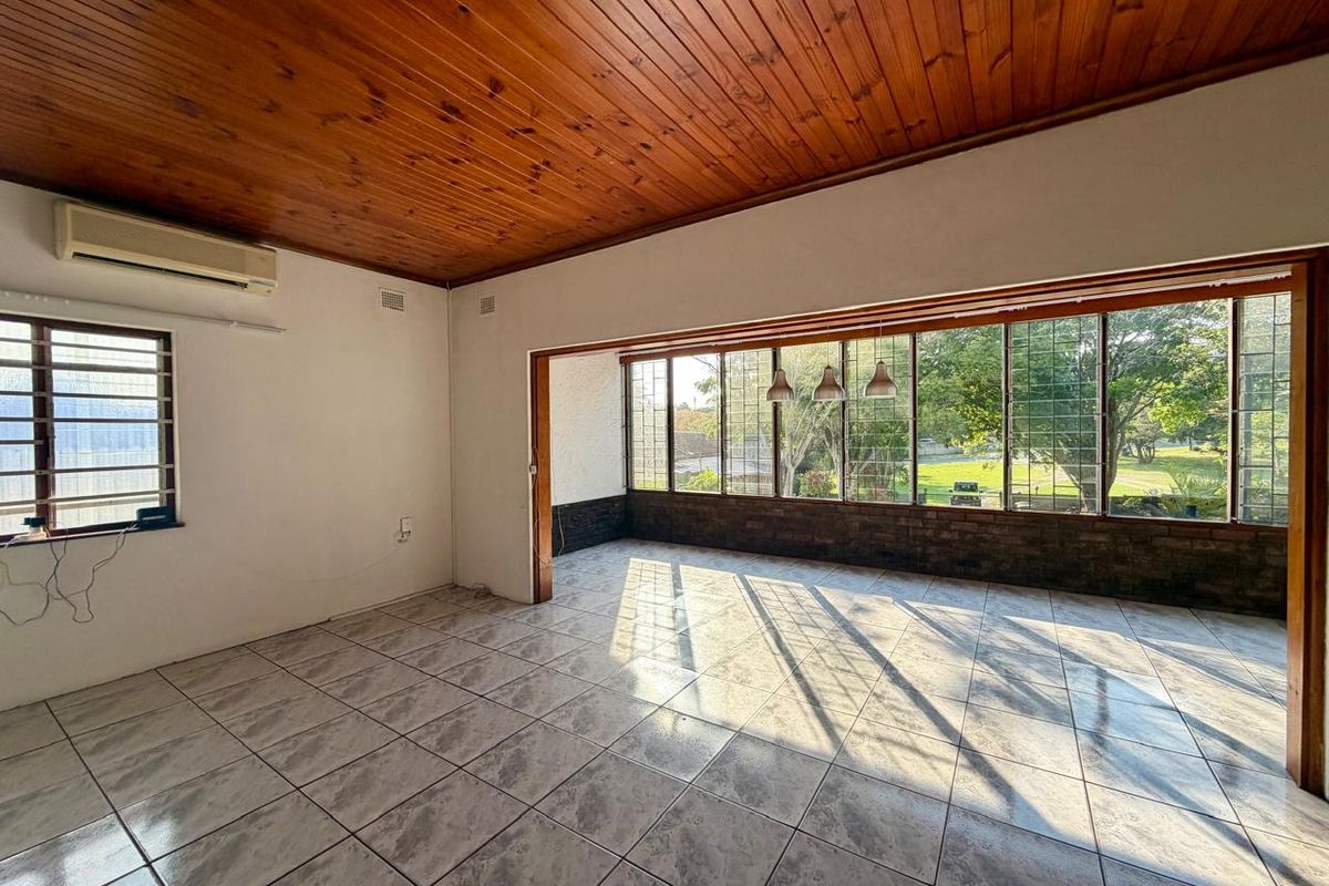 Spacious living area featuring a timber-clad ceiling, ceramic tiled flooring, and large windows providing ample natural light and garden views.