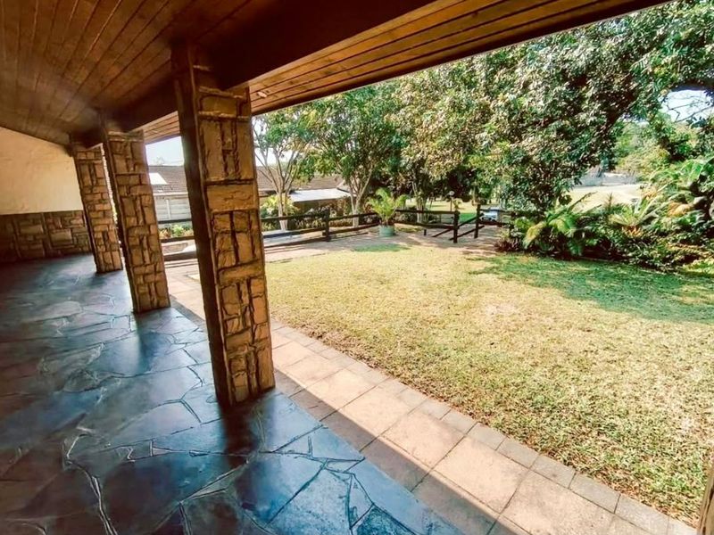 A covered patio featuring flagstone flooring and stone-clad pillars, overlooking a well-maintained garden area.