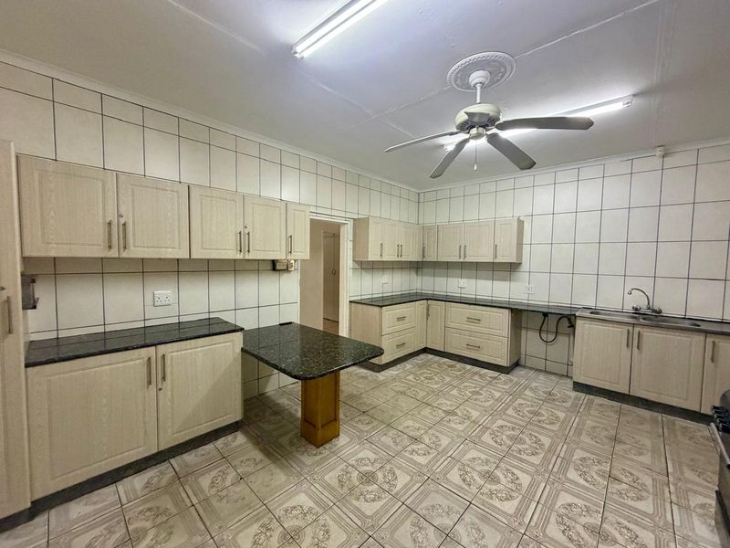 Spacious kitchen featuring extensive built-in cabinetry, granite countertops, double sink, and tiled finishes throughout, offering a functional layout ready for modernization.
