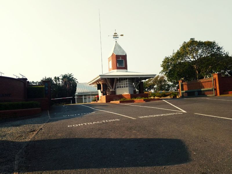 The entrance to the residential estate features a brick security gatehouse, paved driveway with designated lanes, and perimeter brick walling.