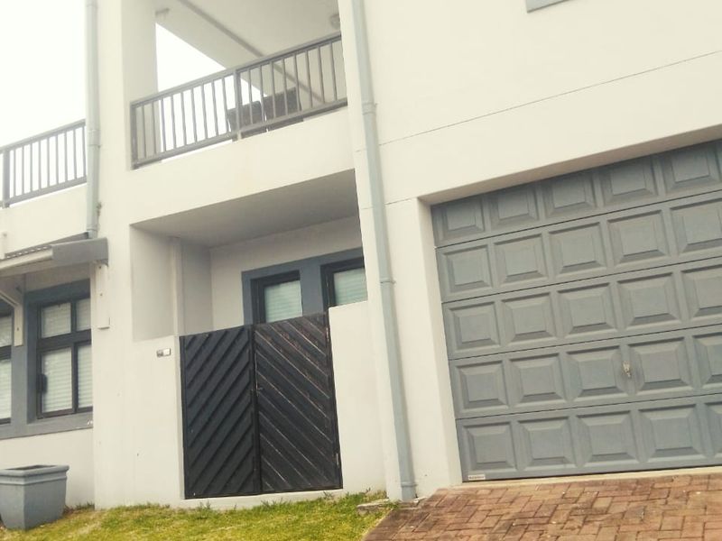 Front elevation of a multi-story residential property featuring a garage, paved driveway, and upper-level balconies with metal railings.