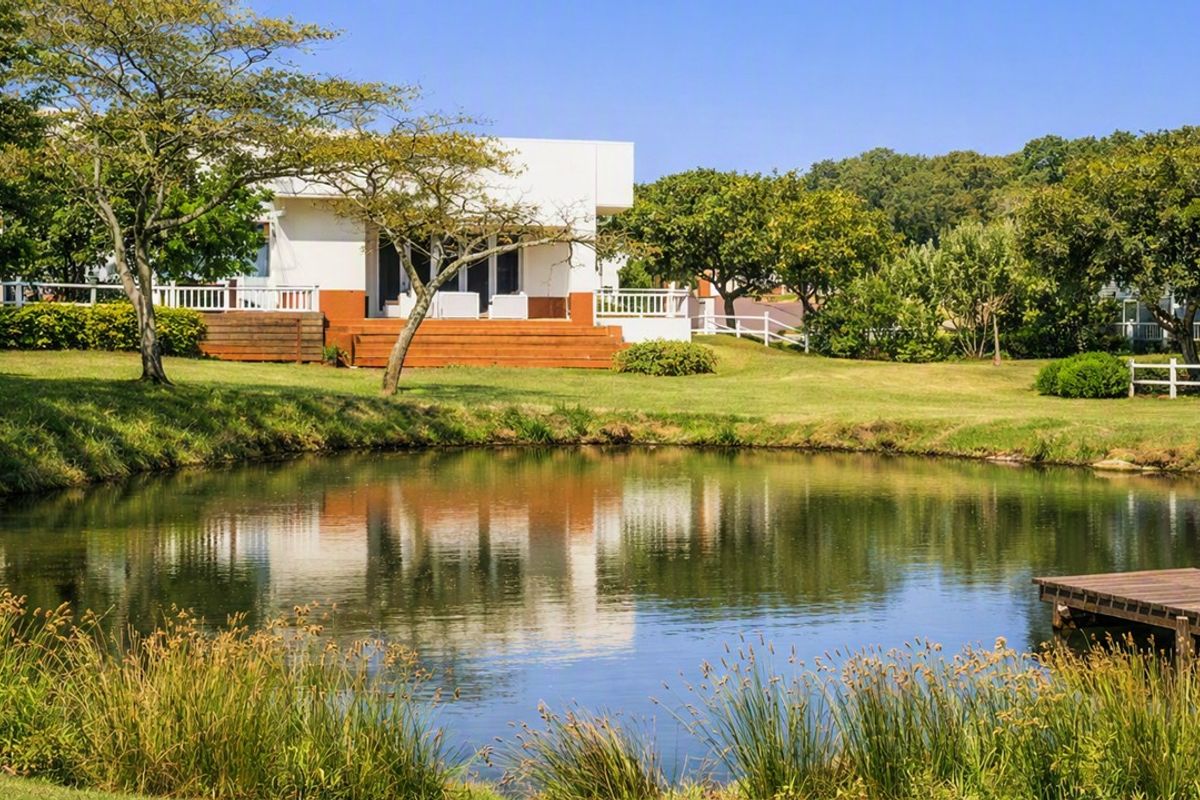 A scenic view of a residential property featuring a well-maintained garden, a tranquil pond with a wooden jetty, and a rear deck.
