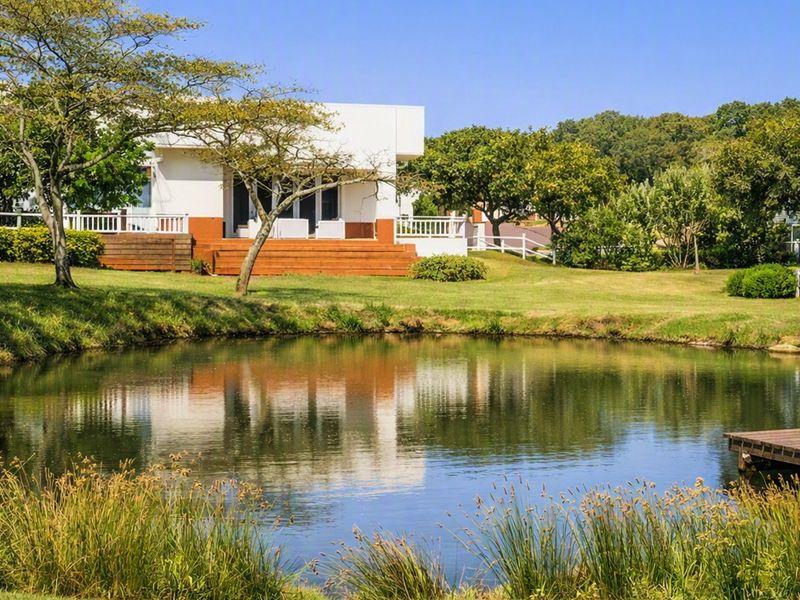 A scenic view of a residential property featuring a well-maintained garden, a tranquil pond with a wooden jetty, and a rear deck.