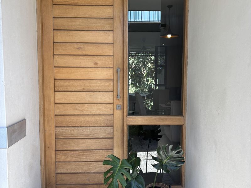 A modern entrance featuring a solid timber front door with a vertical sidelight window and stone paver flooring.