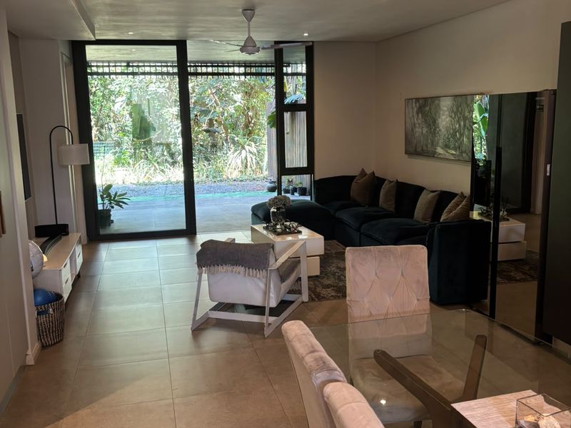 Spacious open-plan living and dining area featuring large format floor tiles, recessed lighting, and expansive sliding glass doors leading to an outdoor patio.