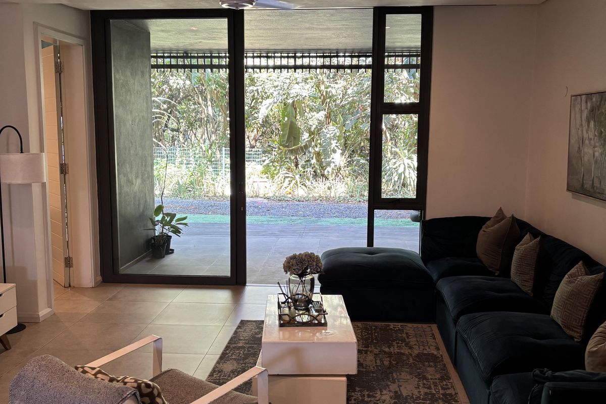 A well-lit living room featuring large sliding glass doors that open onto a patio, tiled flooring, and a modern ceiling fan.