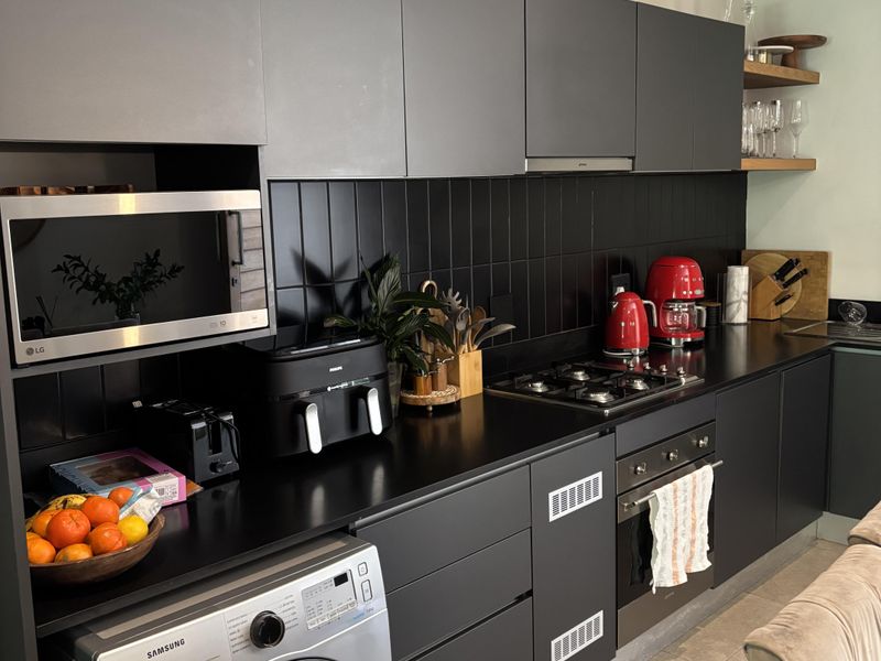 Modern kitchen featuring sleek dark cabinetry, black subway tile backsplash, integrated appliances, and a gas hob with a built-in oven.