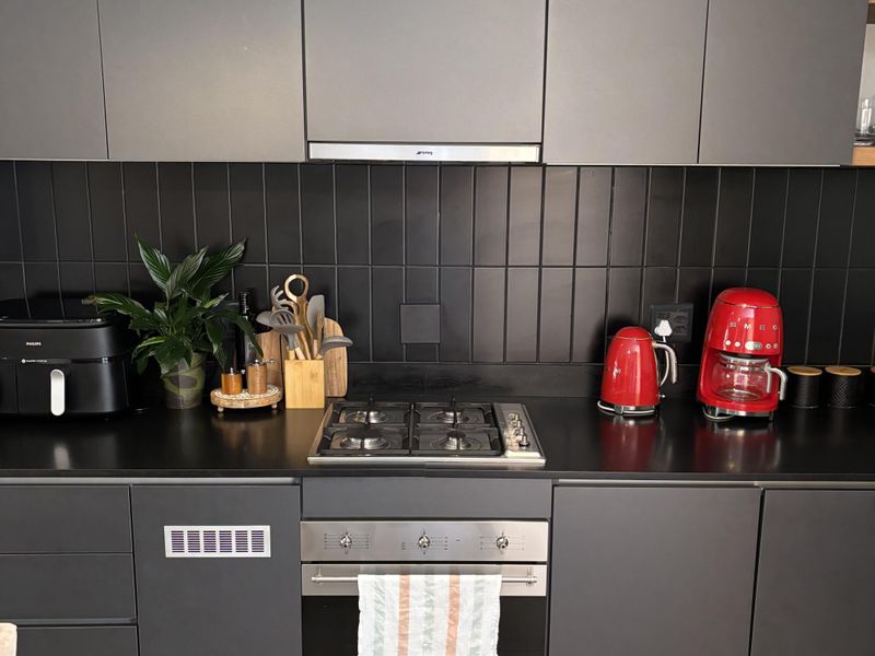 Modern kitchen featuring matte grey cabinetry, a black tiled backsplash, stone countertops, and integrated stainless steel appliances including a gas hob and oven.
