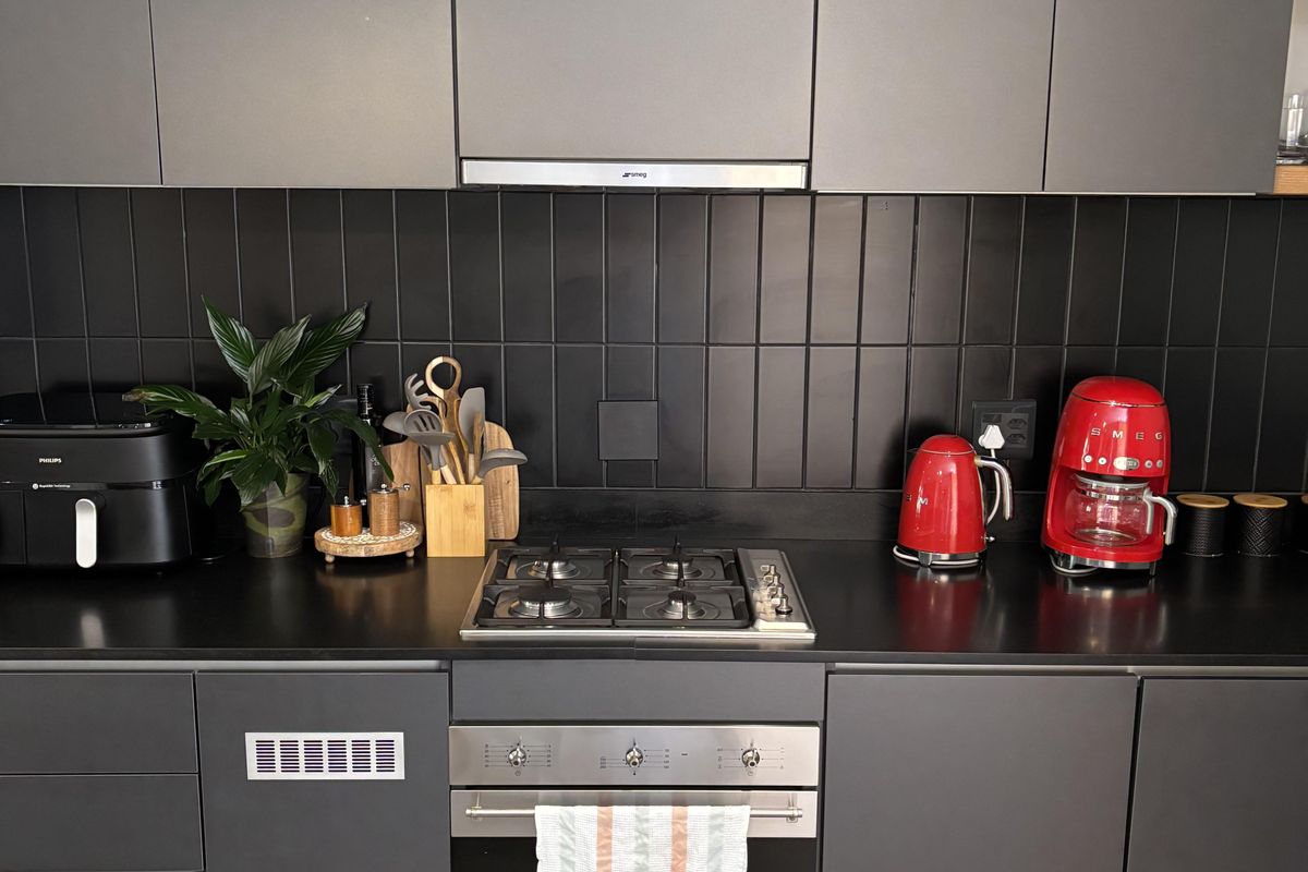 Modern kitchen featuring matte grey cabinetry, a black tiled backsplash, stone countertops, and integrated stainless steel appliances including a gas hob and oven.