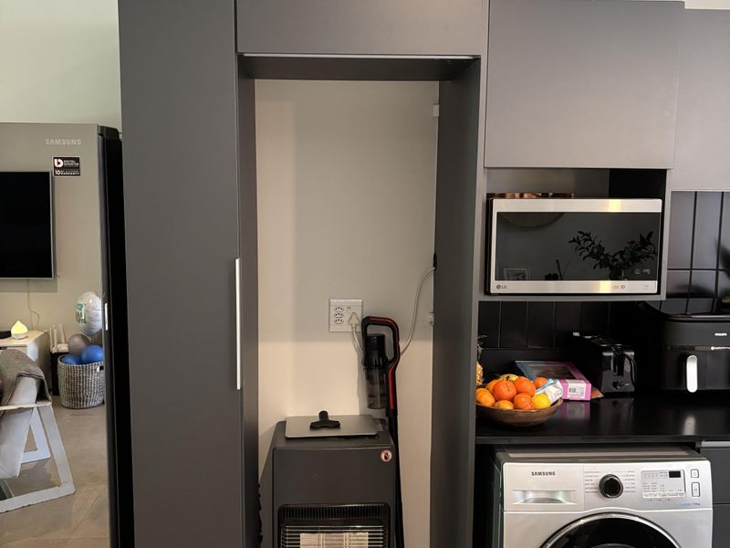 Modern kitchen area featuring dark grey cabinetry, integrated microwave, and tiled backsplash, with visible water staining on the ceiling requiring attention.