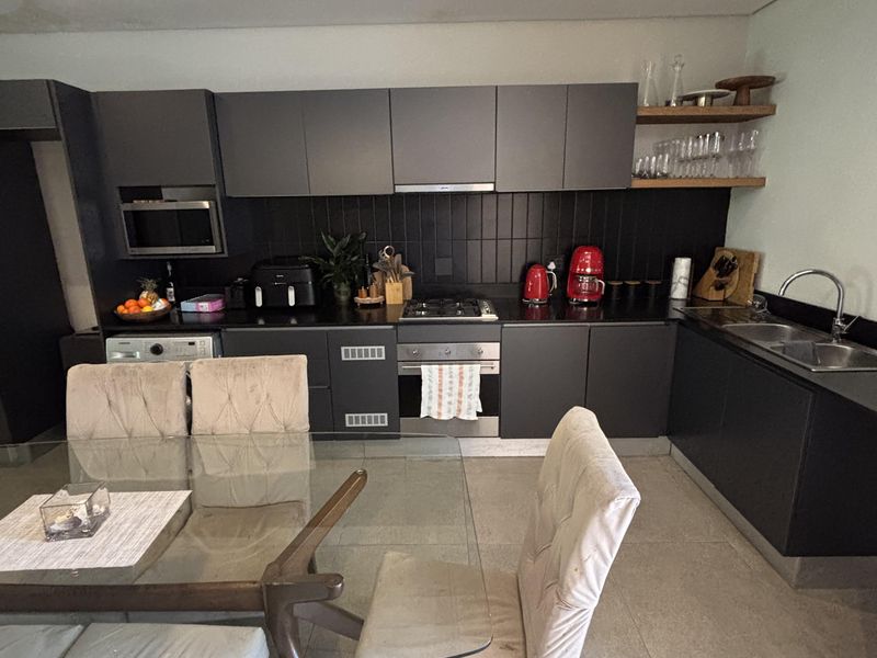 Modern open-plan kitchen featuring dark cabinetry, integrated appliances, gas hob, and sleek tiled flooring, seamlessly flowing into the dining area.