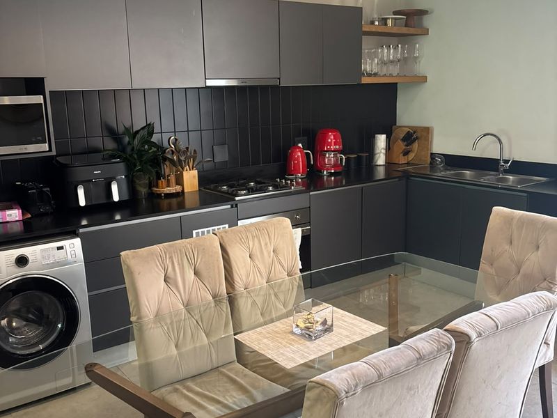 Modern open-plan kitchen featuring dark cabinetry, integrated appliances, gas hob, and a sleek tiled backsplash, seamlessly flowing into the dining area.