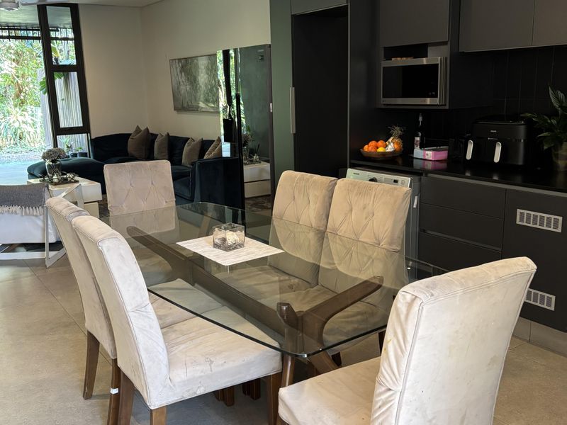 Open plan living and dining area featuring modern dark cabinetry, tiled flooring, and a pendant light, with visible water staining on the ceiling.