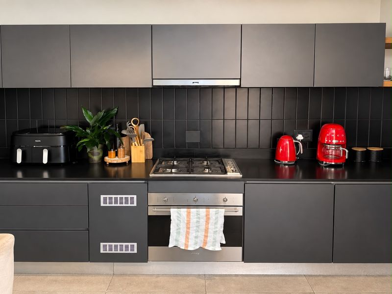 Modern kitchen featuring matte grey cabinetry, a sleek black subway tile backsplash, integrated gas cooktop, and stainless steel oven.