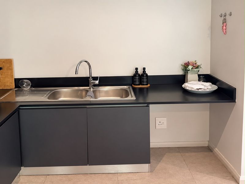 A modern kitchen area featuring dark grey cabinetry, a stainless steel double sink with a chrome mixer tap, and a sleek dark countertop.