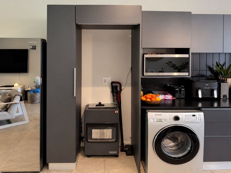 Modern kitchen area featuring dark grey cabinetry, integrated microwave, tiled backsplash, and a built-in washing machine.