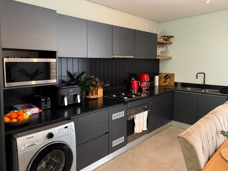 Modern kitchen featuring dark matte cabinetry, integrated appliances, gas hob, built-in oven, and a sleek tiled backsplash with a double sink.