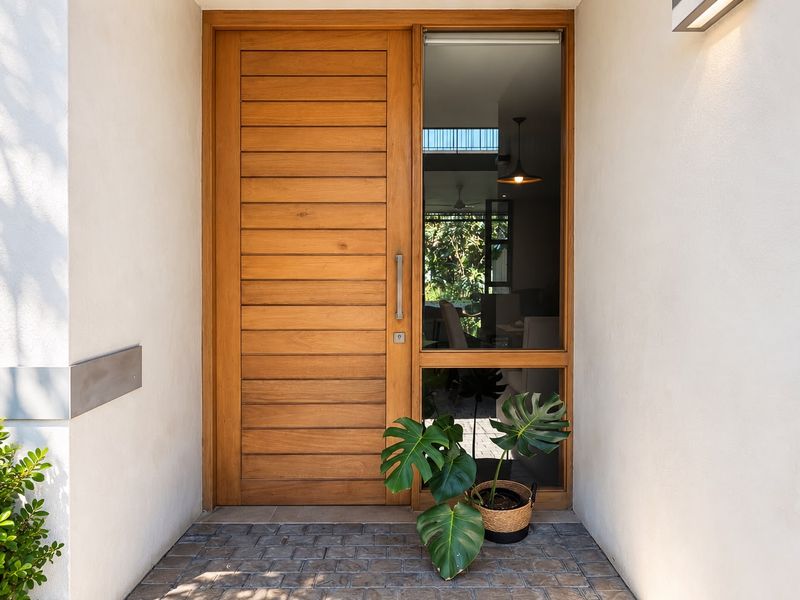 A modern, well-maintained entryway featuring a solid timber front door with a glass sidelight and paved flooring.