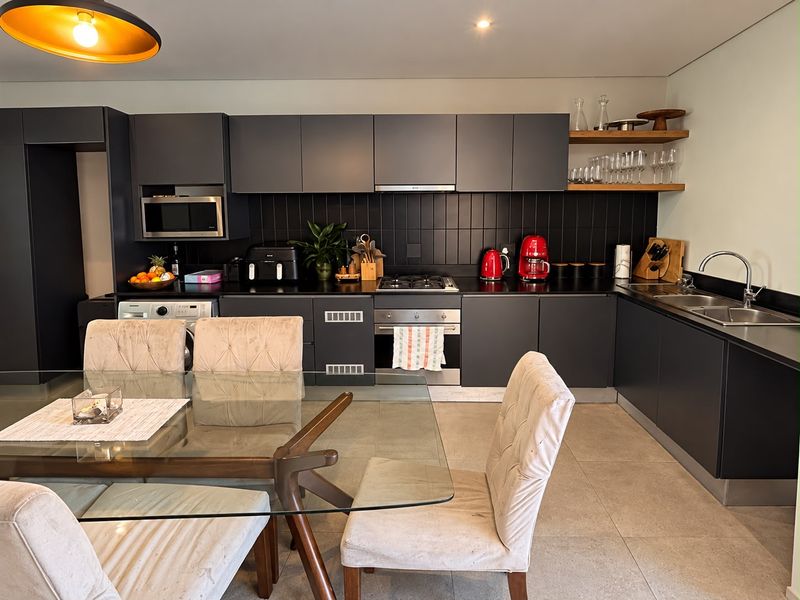 Modern open-plan kitchen featuring sleek dark cabinetry, integrated appliances, gas hob, and tiled finishes, seamlessly flowing into the dining area.