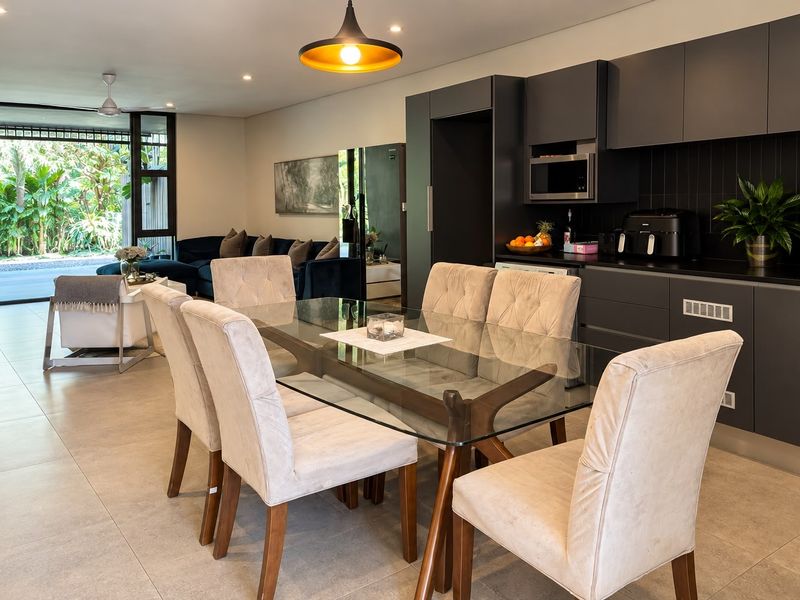 Modern open-plan living and dining area featuring sleek dark cabinetry, tiled floors, and seamless access to the outdoor patio through large sliding glass doors.