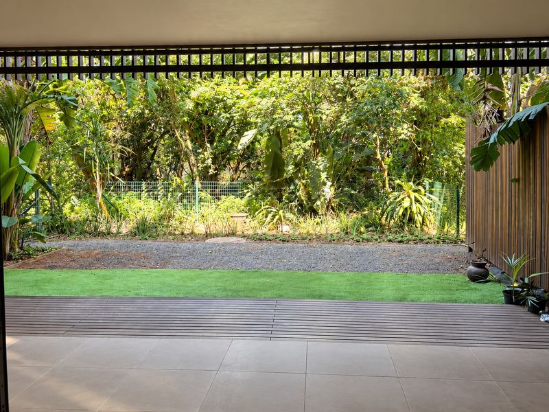 A covered patio area featuring tiled flooring, timber decking, and artificial turf, overlooking a private garden with lush greenery and a privacy screen.