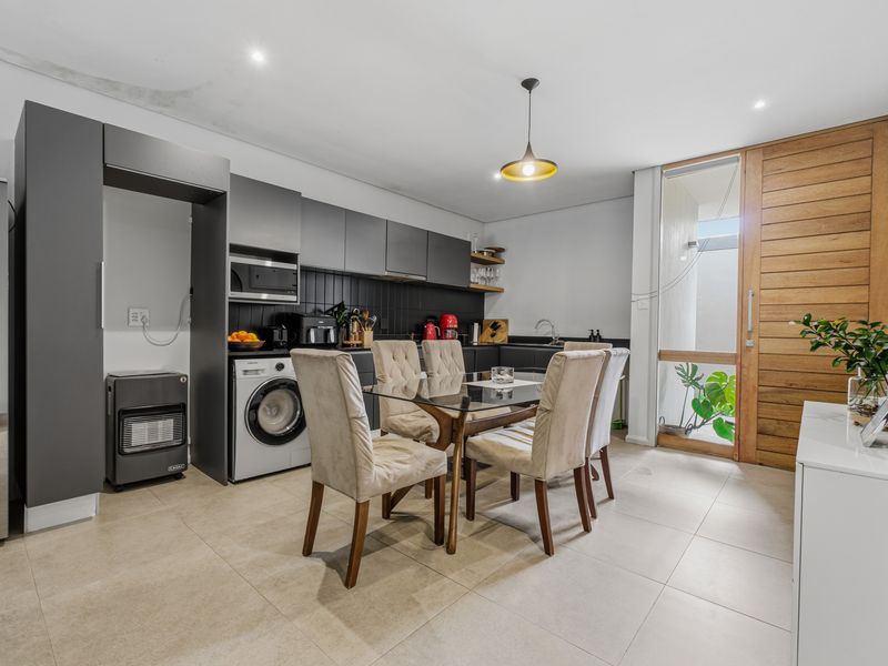 Open-plan kitchen and dining area featuring modern dark cabinetry, integrated laundry appliances, tiled flooring, and direct access to an outdoor space.